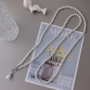 Detailed shot of long pearl waist chain necklace with baroque pendant and metal clasp.