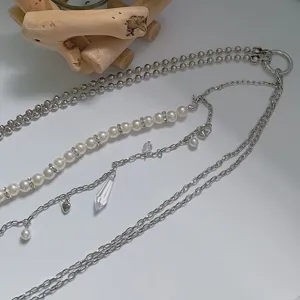 Close-up detail of a layered metal and pearl body chain with a crystal drop pendant.