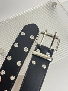 Close-up detail of black punk style double grommet belt with silver metal double prong buckle.