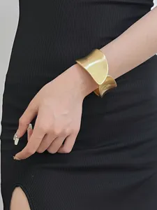 Detailed view of wide brushed gold cuff bracelet, modern minimalist open bangle jewelry.