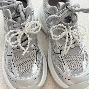 Silver sneakers detail close-up with elegant pearl bow shoe charms, fashion footwear decor.