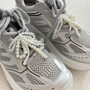 Close-up detail of silver mesh sneakers decorated with elegant handmade pearl bow shoe charms.