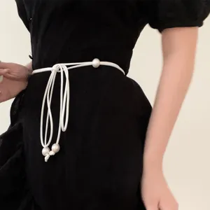 Close-up of a minimalist white cord waist belt with elegant pearl accents on a black dress.