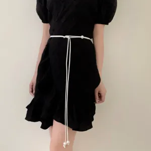 Detail shot of a minimalist white cord belt with elegant pearl ends worn on a black dress.