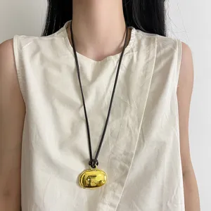 Detail shot of the minimalist long sweater chain with gold oval pendant and brown cord.