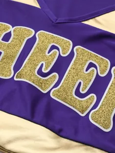 Cheerleading uniform apparel close up detail, purple gold fabric with glitter letter print design.
