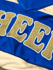 Cheerleading uniform top detail shot, blue and gold metallic fabric with glitter letters.