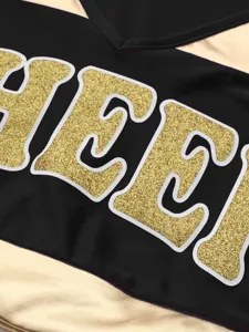 Detailed view of the cheerleading performance costume top with gold glitter lettering and V-neck.
