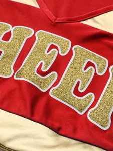 Close-up detail of red and gold cheerleading uniform top with sparkly glitter letter print.
