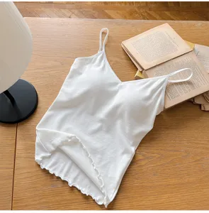 Detailed view of white ribbed V-neck camisole with chest pad and lettuce trim on wood table.