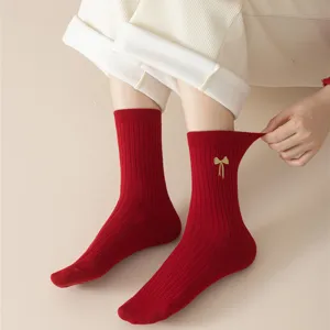 Close up view of red ribbed knit cotton socks featuring a delicate gold bow embroidery