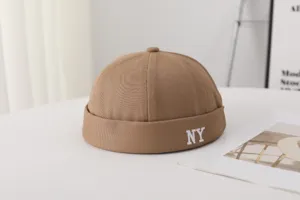 Gros plan d'un bonnet docker khaki avec broderie blanche NY, configuration de table minimaliste.
