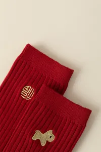 Red cotton knit sock detail close up showing gold embroidered lucky character and cute animal.