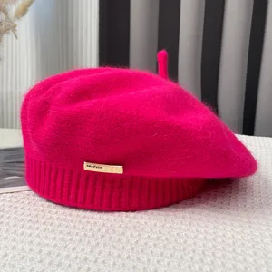 Detailed view of a bright pink knitted beret with cute tail design and sleek metal hardware tag.
