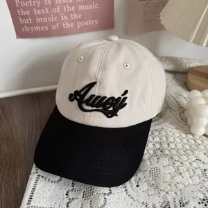 Detail view of a stylish two-tone baseball cap with black embroidered cursive lettering and brim.