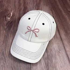 Casquette de baseball blanche élégante avec surpiqûres noires et joli nœud rose.
