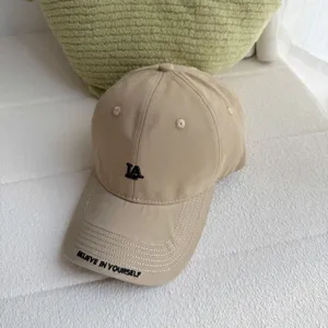 Close-up view of the beige baseball cap showcasing front LA embroidery and brim letter details.