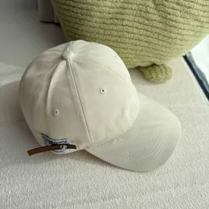 Minimalist off-white baseball cap detail with soft fabric and chic side leather strap.