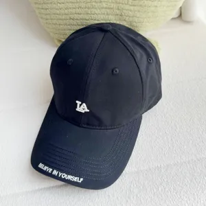 Black baseball cap detail with LA embroidery and brim text, casual streetwear style.