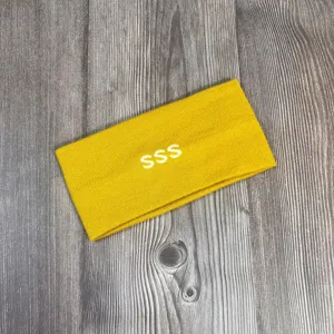 Detail van gele gebreide hoofdband met witte SSS borduursel en zachte, comfortabele textuur.