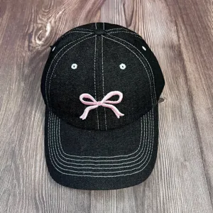 Casquette de baseball en denim noir avec nœud brodé rose et coutures contrastées.
