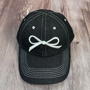 Vue détaillée de la casquette de baseball en denim noir avec broderie nœud blanc et surpiqûres.