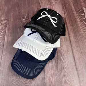 Vue détaillée de casquettes de baseball en denim lavé avec broderie nœud en superposition.