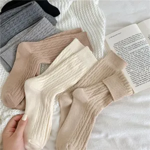 Close-up detail of cozy cable-knit winter women's socks in warm neutral colors on a soft blanket.