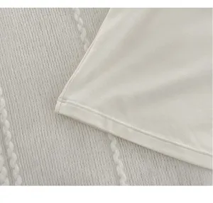Close-up detail of smooth silk knit camisole fabric and neat hem edge in soft neutral tone.