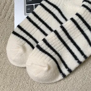 Detailed view of thick warm striped women socks in white and black, cozy wool-blend fabric.
