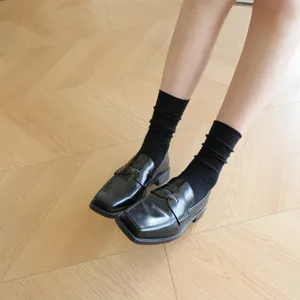 Detailed view of black ribbed mid-calf cotton socks paired with stylish leather loafers.