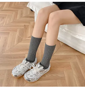 Dettaglio di calze al polpaccio da donna a treccia in grigio scuro abbinate a sneakers.