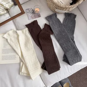 Knitted wool leg warmers, long slouchy stirrup socks in white, brown, and grey. Cozy knit texture.