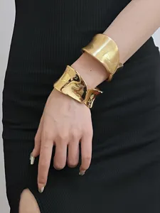 Detailed shot of wide open gold bangles, featuring polished and brushed irregular textures.