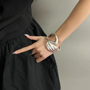Close-up detail of a minimalist wide silver metal open cuff bracelet, sculptural style.