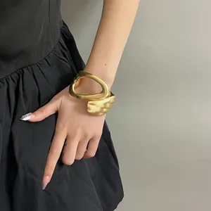 Wide geometric cutout gold cuff bracelet, minimalist matte metallic finish, chic hand detail view.