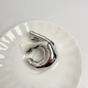 Detailed view of a silver metal OK gesture brooch, stylish minimalist fashion pin accessory.