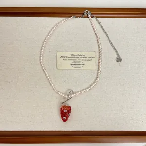 Detailopname van roze parelketting met rode aardbei hanger en metalen ketting details.