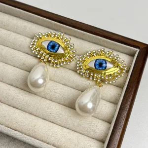 Détail boucles d'oreilles perle œil bleu vintage, bijoux de luxe rétro en strass et or.