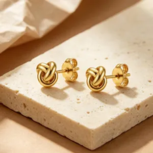 Close-up view of elegant golden knot stud earrings on a textured stone surface