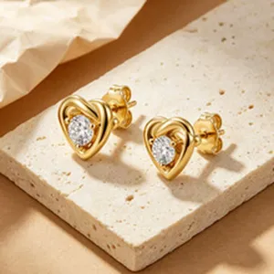 Macro view of elegant gold heart stud earrings with zircon on a travertine slab