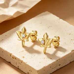 Detail shot of gold maple leaf stud earrings with center zircon on a textured stone