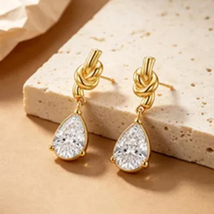 Macro detail of elegant gold-plated knot earrings with clear pear-shaped zircon dangle