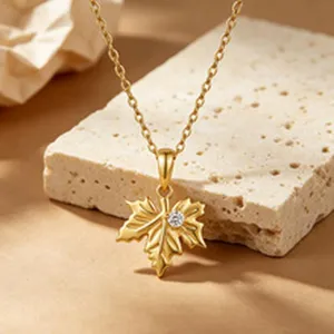 Detailed close-up of gold maple leaf pendant necklace with shimmering zircon accent