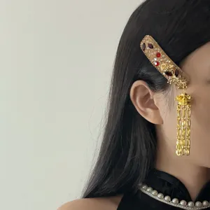 Elegant gold side hair clip with sparkling red gems and long dangling chains for women.