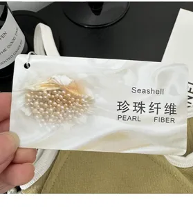Close-up detail of the seashell pearl fiber camisole product tag, ribbed knit fabric texture.