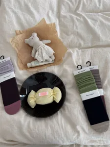 Cozy cotton colorblock crew socks detail shot with aesthetic props on beige bedding.