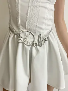 Vista di dettaglio della cintura catena vita con lettere in metallo, design elegante.
