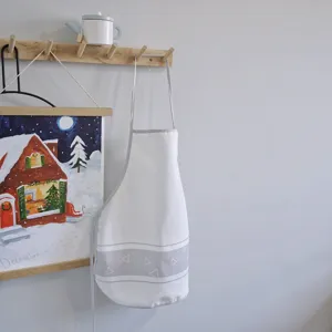 Children apron detail shot featuring white fabric with grey geometric pattern hanging on hook.