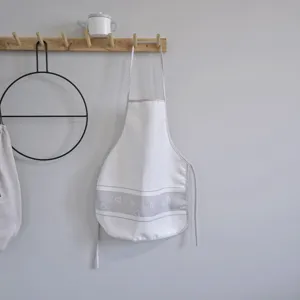Detail shot of a minimalist white apron with grey geometric patterns on a wooden rack.